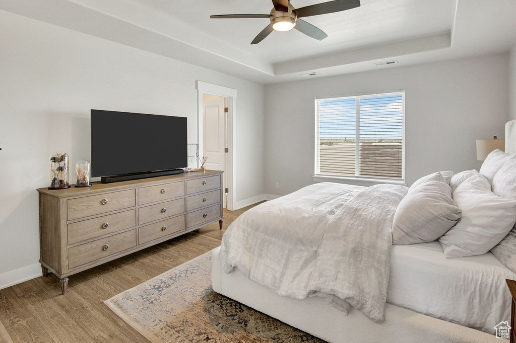 Bedroom with a raised ceiling, light wood-type flooring, and ceiling fan