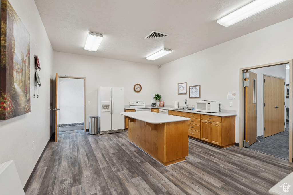 Kitchen with white appliances, light countertops, a center island, and dark wood-type flooring