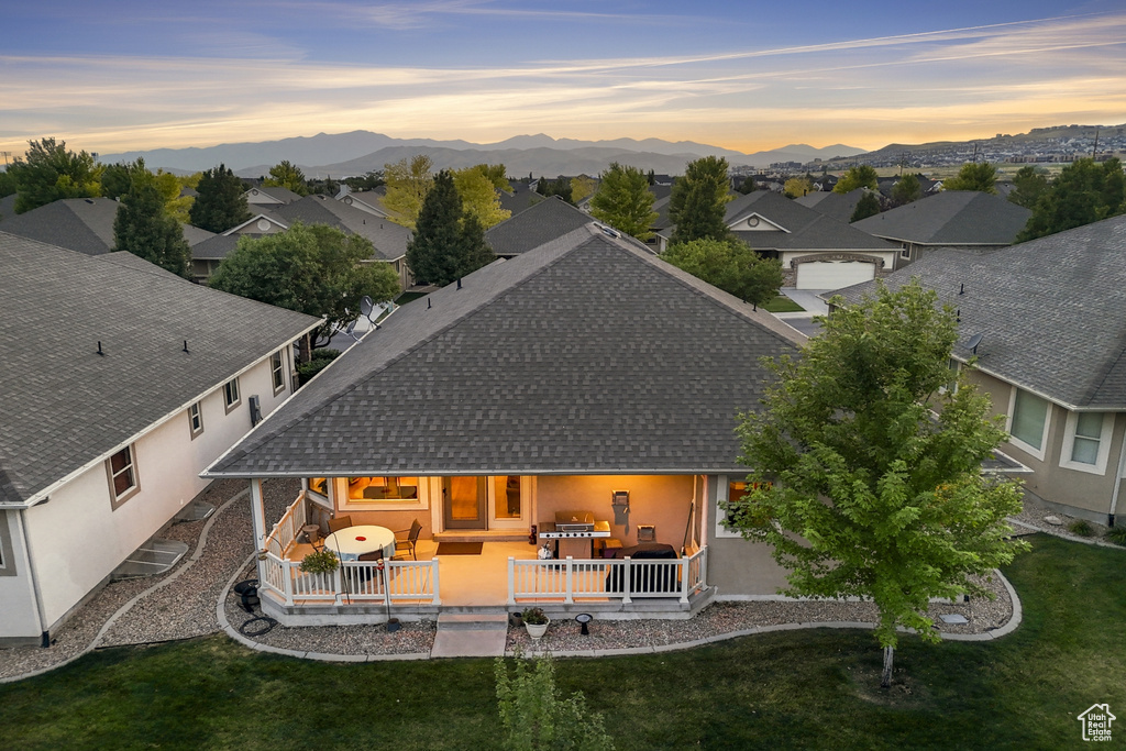 Back of property at dusk featuring roof with shingles, a deck with mountain view, a yard, stucco siding, and a residential view