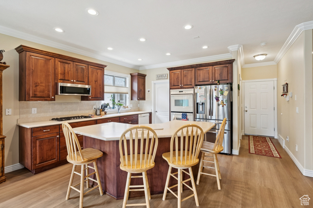 Kitchen featuring appliances with stainless steel finishes, a kitchen island, light wood-style flooring, light countertops, and ornamental molding