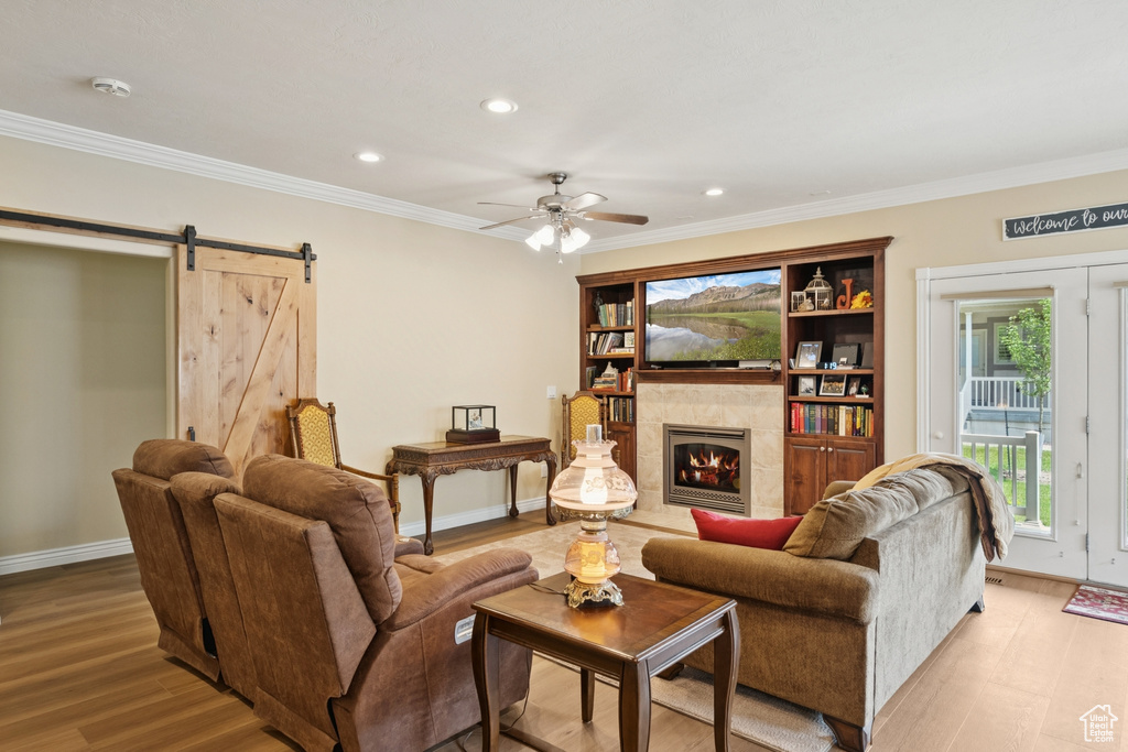 Living room with a ceiling fan, crown molding, light wood-style flooring, a tiled fireplace, and recessed lighting