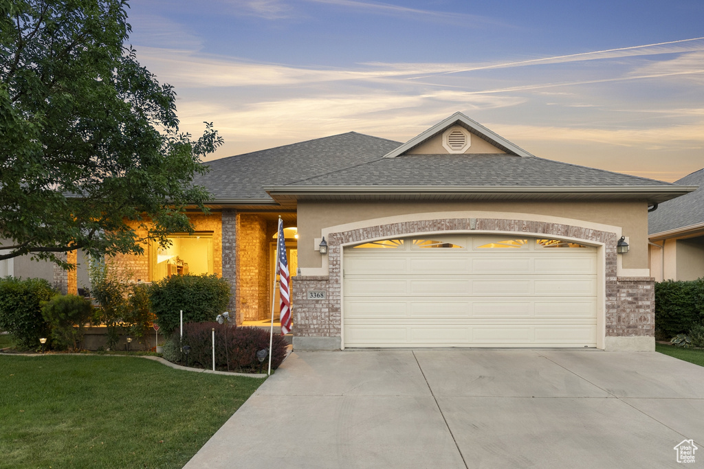 View of front facade with a garage, concrete driveway, a yard, roof with shingles, and stucco siding