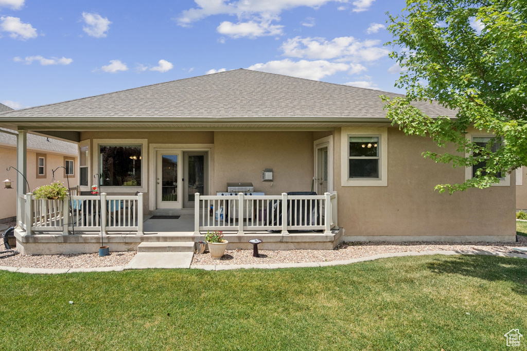 Rear view of house with a shingled roof, stucco siding, and a yard