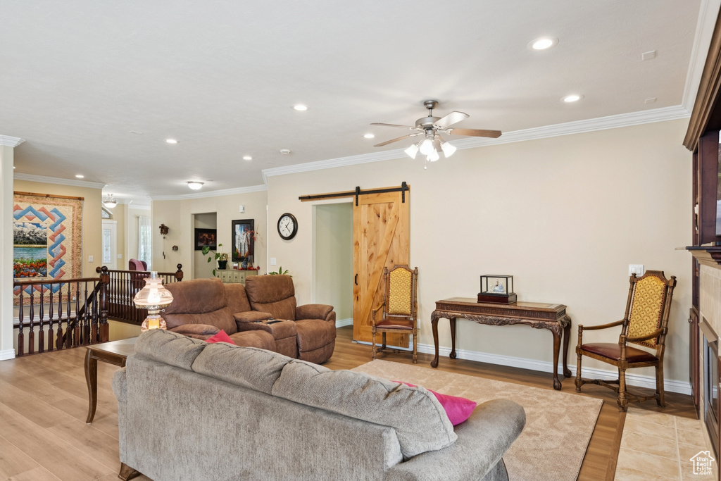 Living room with a barn door, light wood-type flooring, recessed lighting, crown molding, and ceiling fan