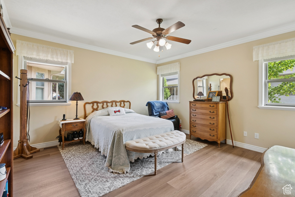 Bedroom featuring light wood-style floors, multiple windows, ornamental molding, and a ceiling fan
