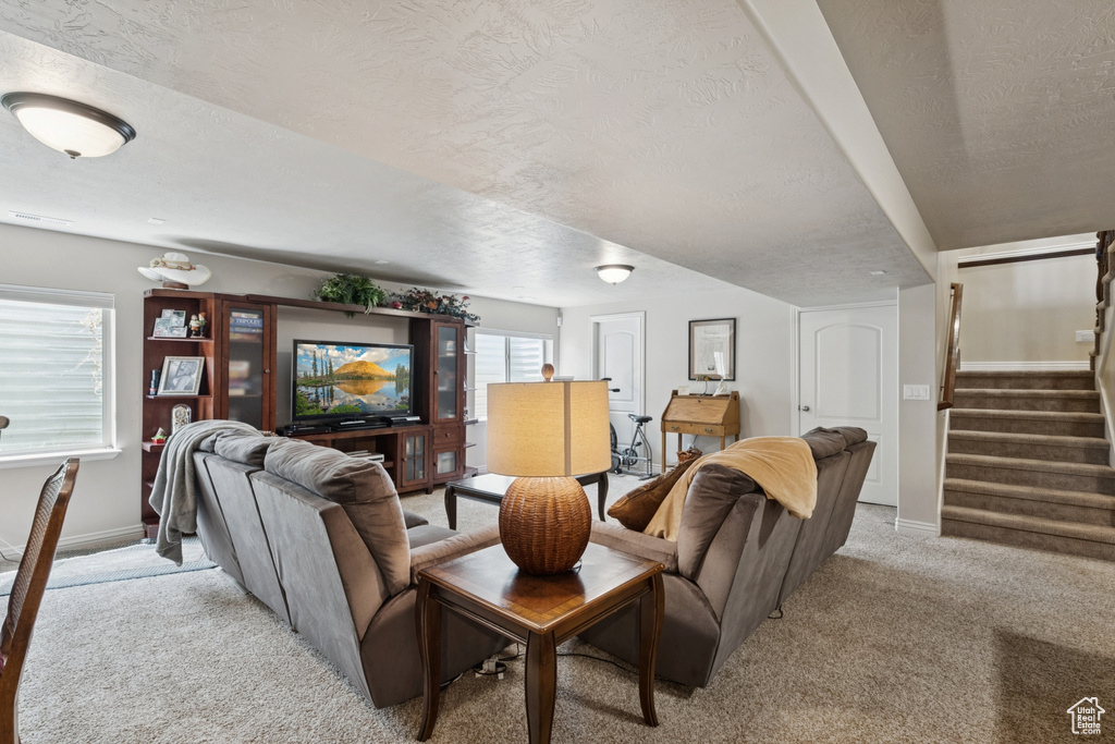 Living area with light colored carpet, a textured ceiling, and stairway