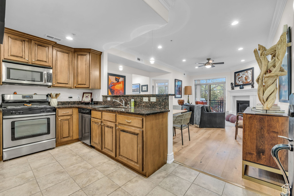 Kitchen featuring appliances with stainless steel finishes, a peninsula, brown cabinetry, ornamental molding, and ceiling fan