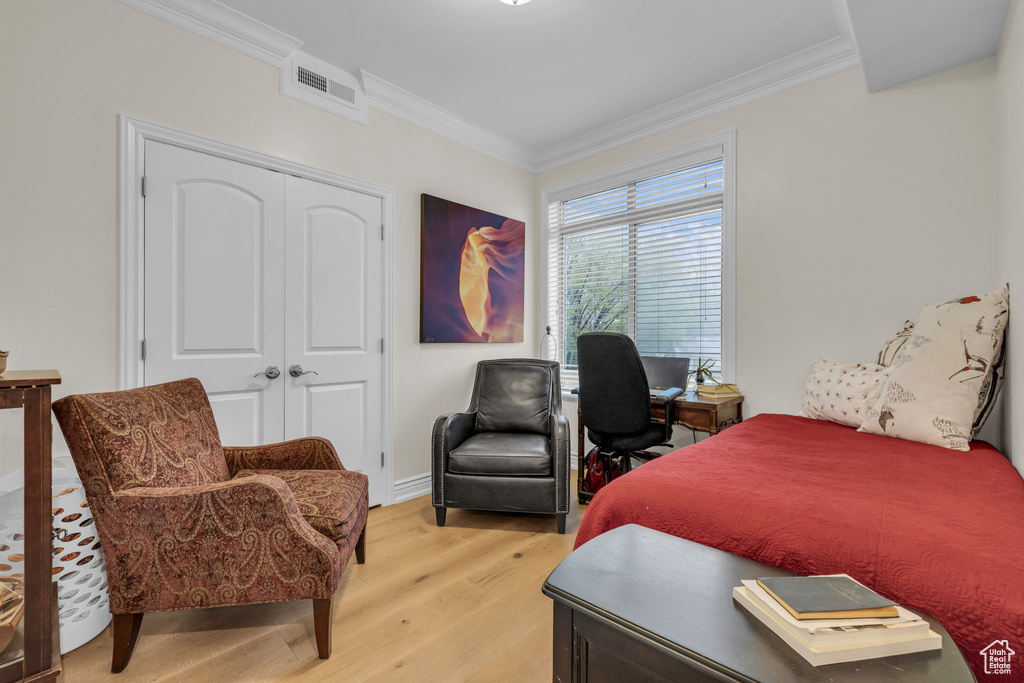 Bedroom with light wood-style floors, crown molding, and a closet