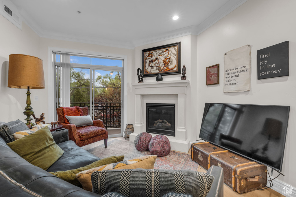 Living room with ornamental molding, wood finished floors, a glass covered fireplace, and recessed lighting