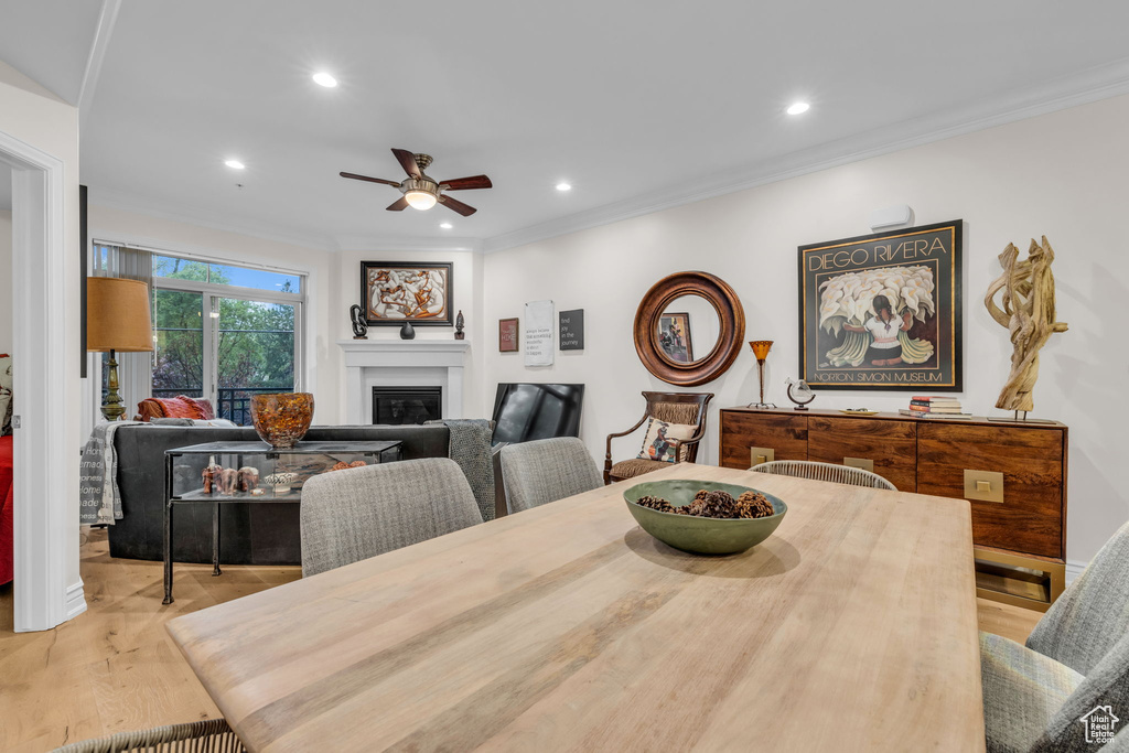Dining area with ceiling fan, a glass covered fireplace, recessed lighting, wood finished floors, and crown molding