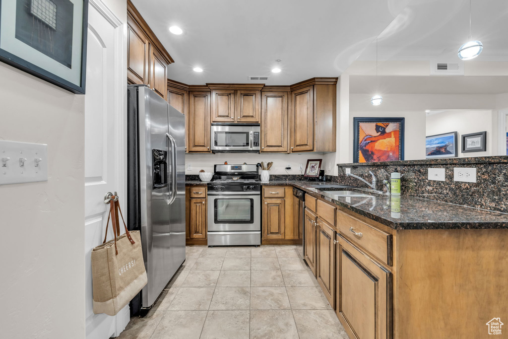 Kitchen with brown cabinetry, appliances with stainless steel finishes, a peninsula, dark stone countertops, and recessed lighting