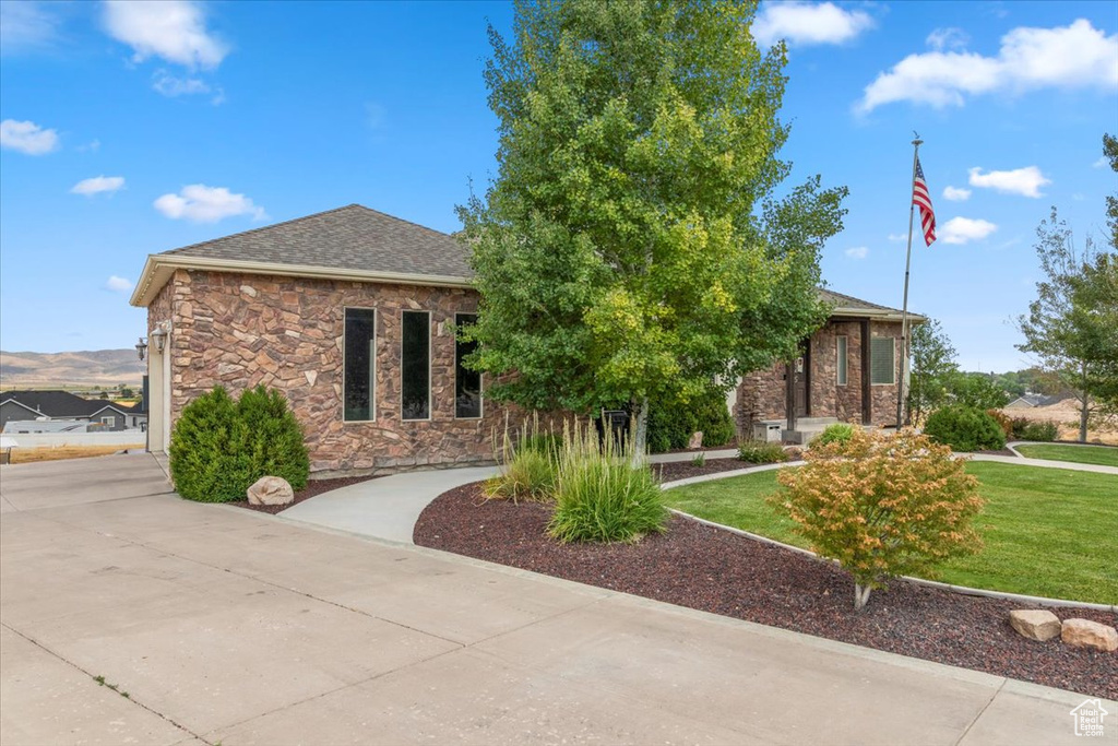 View of front of home featuring concrete driveway, a front yard, stone siding, and roof with shingles