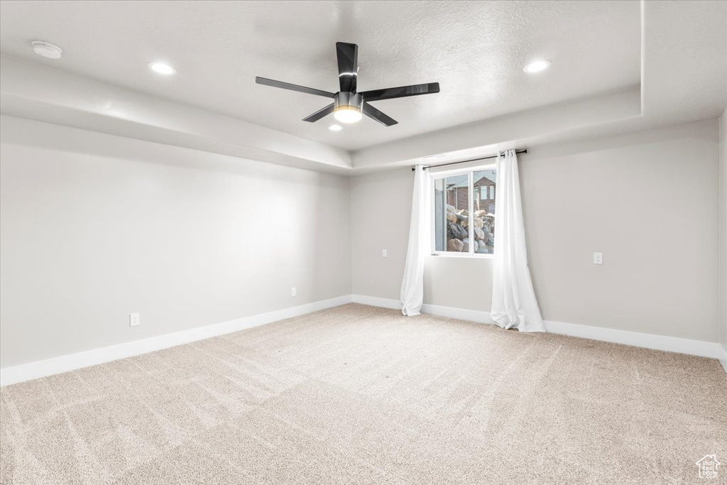 Empty room with ceiling fan, light colored carpet, recessed lighting, and a raised ceiling