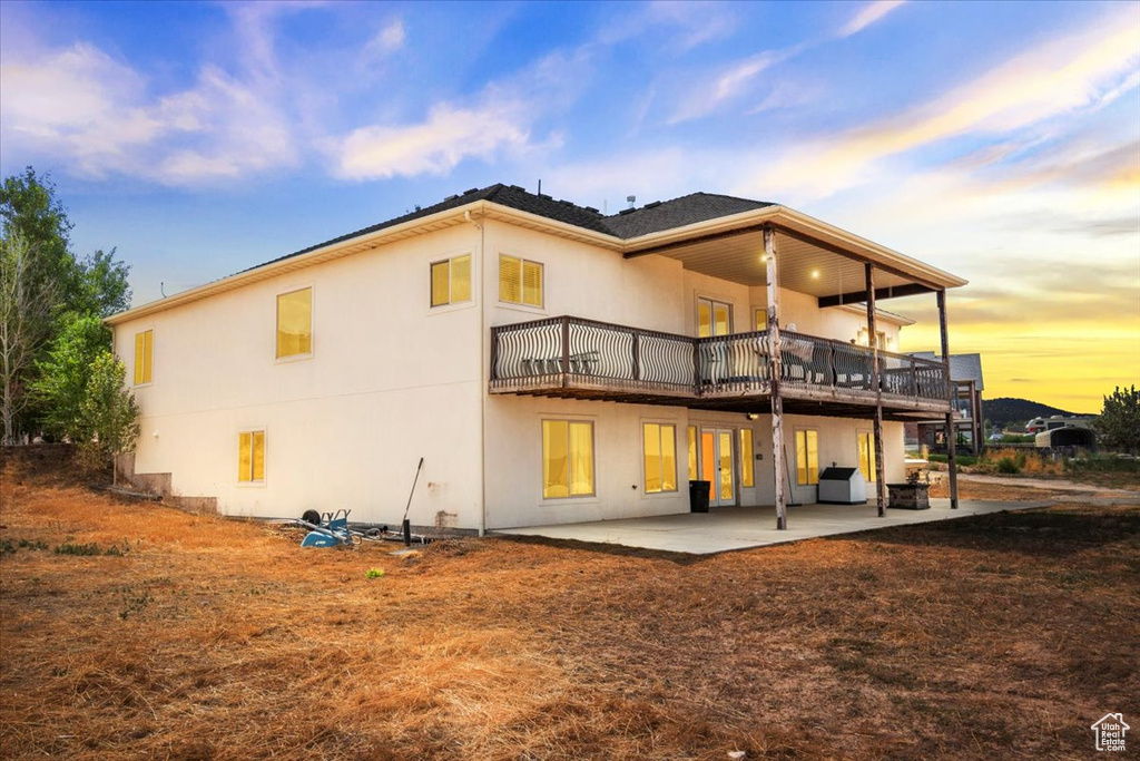 Back of property at dusk with a patio, stucco siding, and a deck