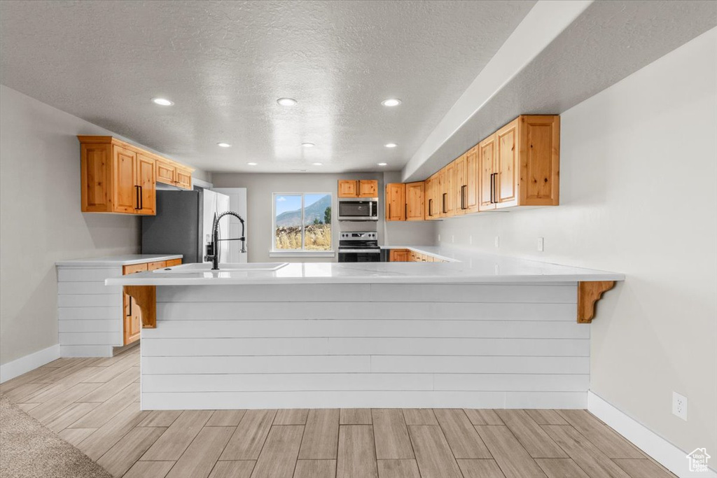 Kitchen with wood finish floors, a textured ceiling, light countertops, a peninsula, and recessed lighting