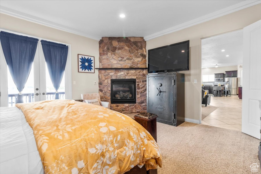 Bedroom featuring crown molding, a stone fireplace, multiple windows, stainless steel refrigerator with ice dispenser, and tile patterned floors