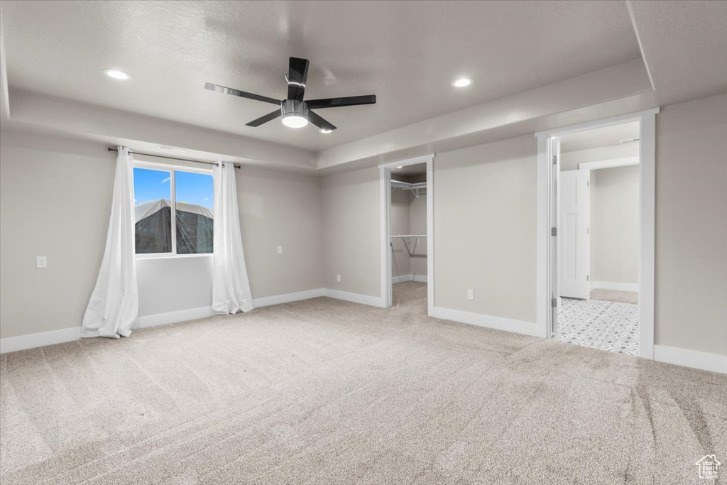 Unfurnished bedroom featuring carpet floors, a walk in closet, recessed lighting, a tray ceiling, and a ceiling fan