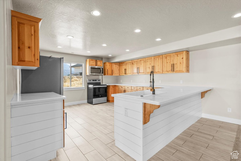 Kitchen featuring a peninsula, stainless steel appliances, a textured ceiling, recessed lighting, and light countertops