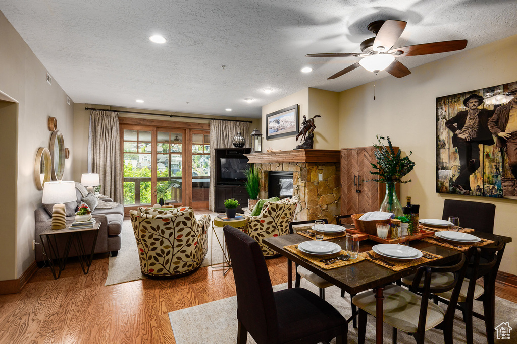 Dining area featuring wood finished floors, a ceiling fan, a stone fireplace, a textured ceiling, and recessed lighting
