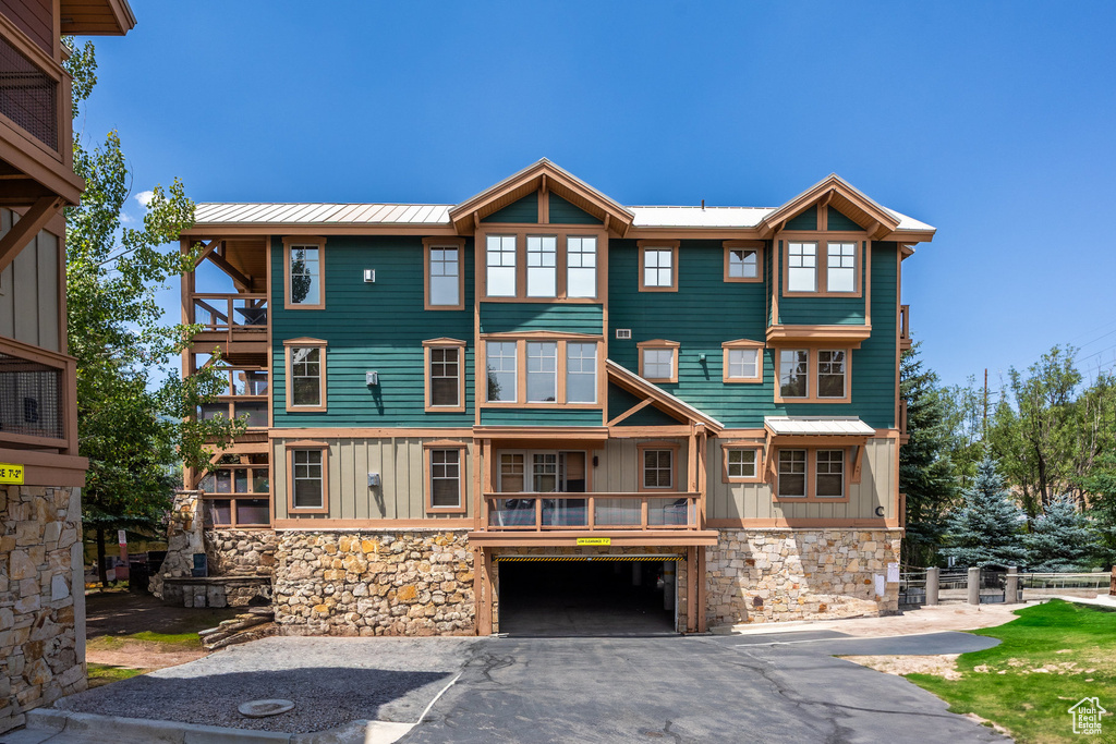View of front of property featuring board and batten siding, stone siding, a balcony, and an attached garage