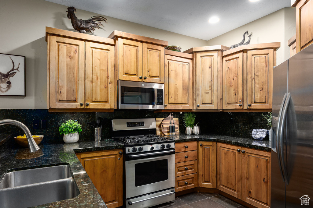 Kitchen with appliances with stainless steel finishes, tasteful backsplash, dark tile patterned flooring, dark stone counters, and recessed lighting