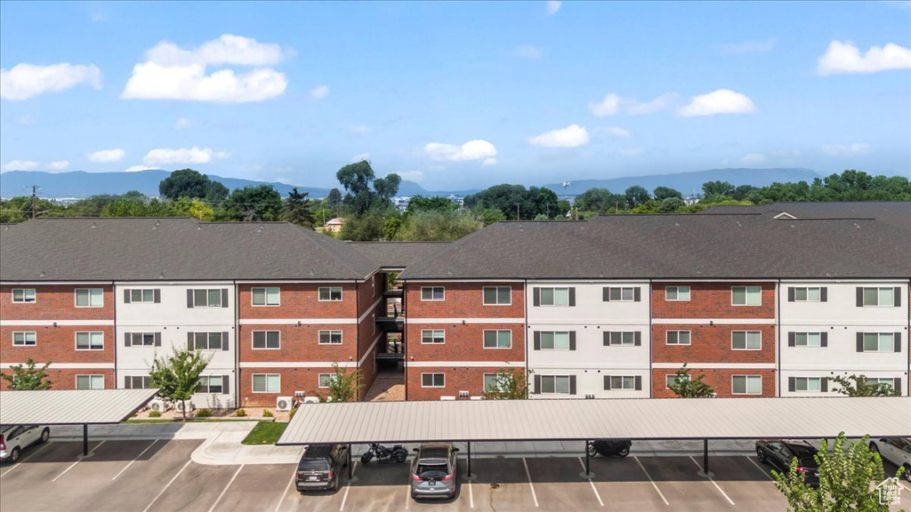 View of building exterior with covered and uncovered parking and a mountain view