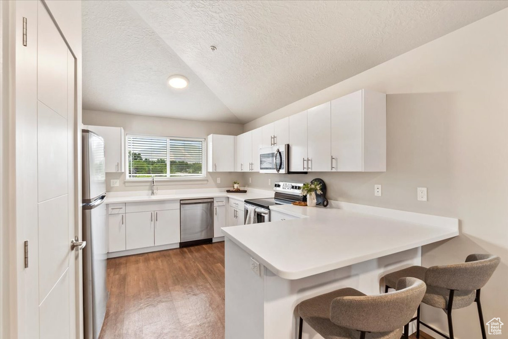 Kitchen with stainless steel appliances, a peninsula, a breakfast bar, vaulted ceiling, and a textured ceiling