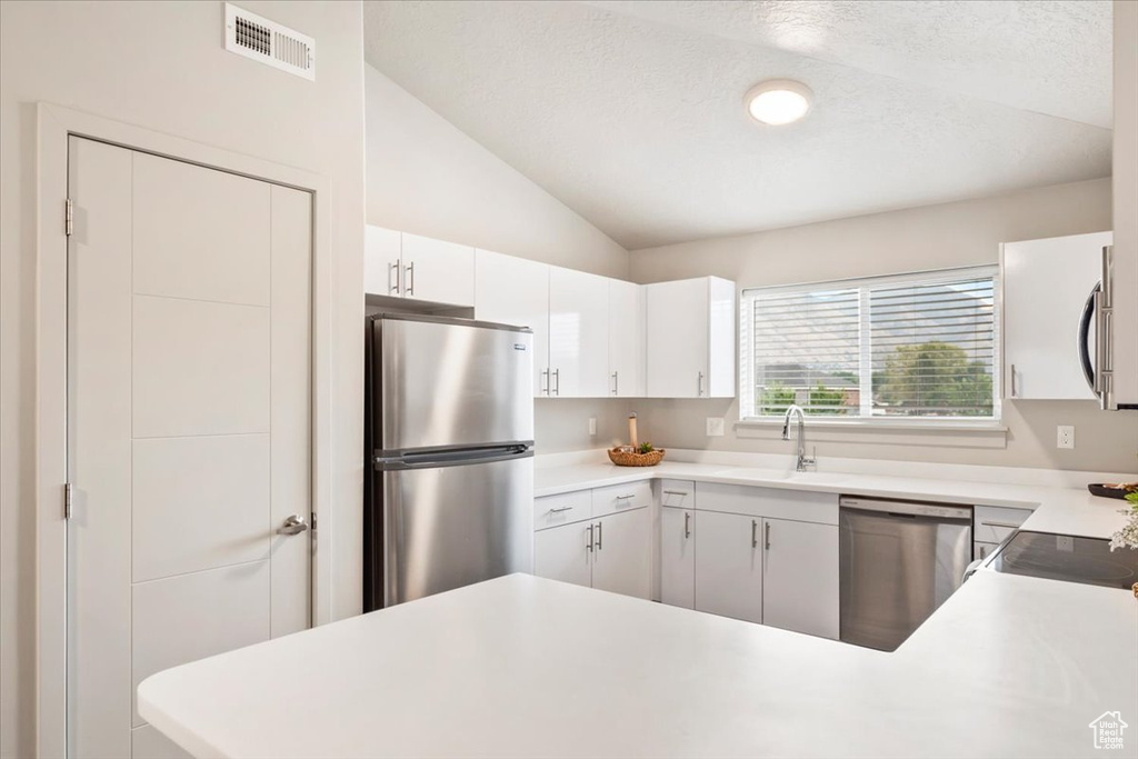 Kitchen with vaulted ceiling, appliances with stainless steel finishes, white cabinets, light countertops, and a peninsula
