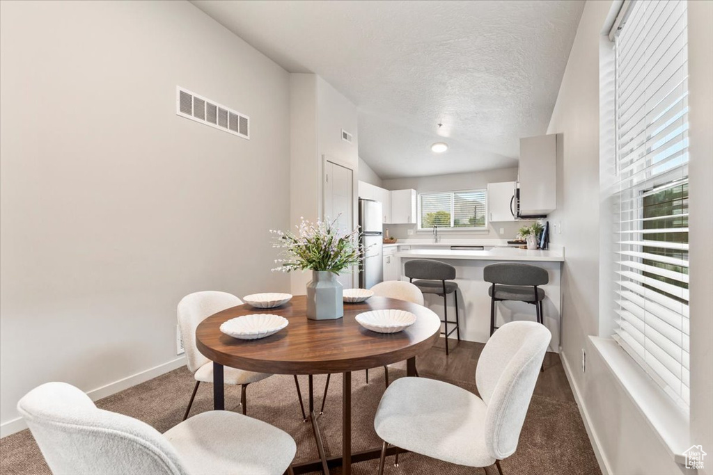 Dining area featuring dark carpet, vaulted ceiling, and a textured ceiling
