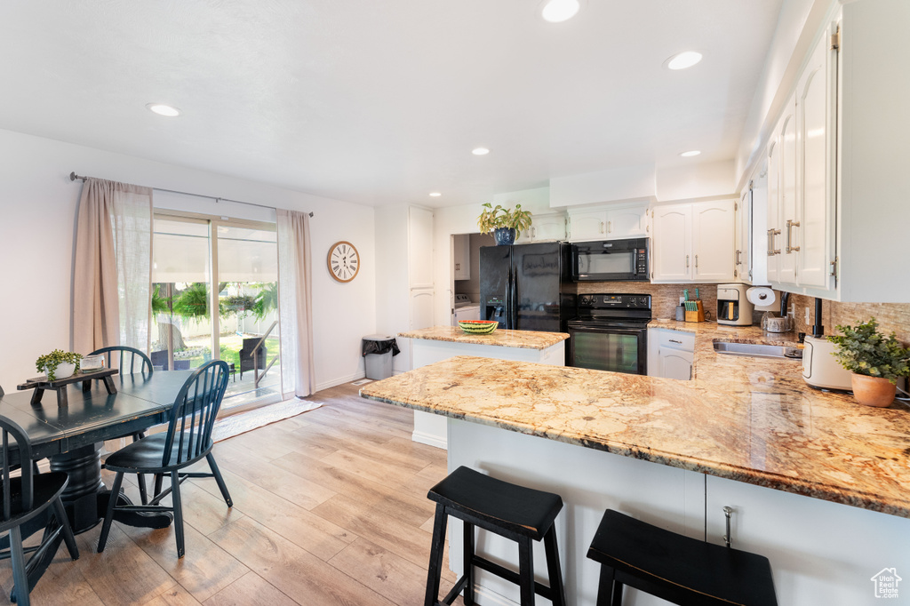 Kitchen with a peninsula, black appliances, light stone countertops, light wood-type flooring, and decorative backsplash