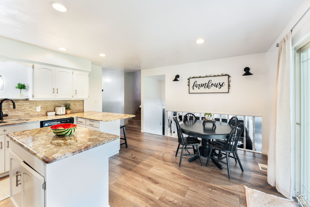 Kitchen with white cabinets, light wood-style flooring, backsplash, a kitchen island, and a peninsula