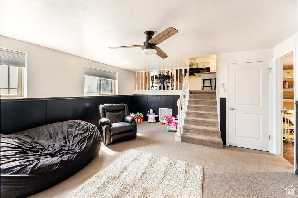 Living area with carpet, a ceiling fan, and stairway