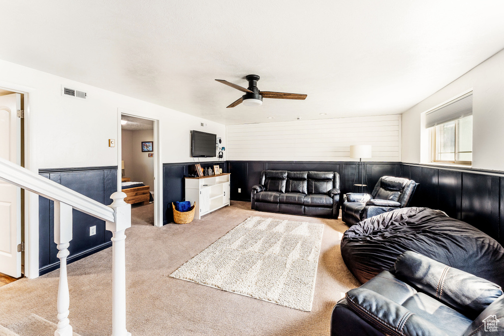Living room featuring ceiling fan, light carpet, a wainscoted wall, and stairs