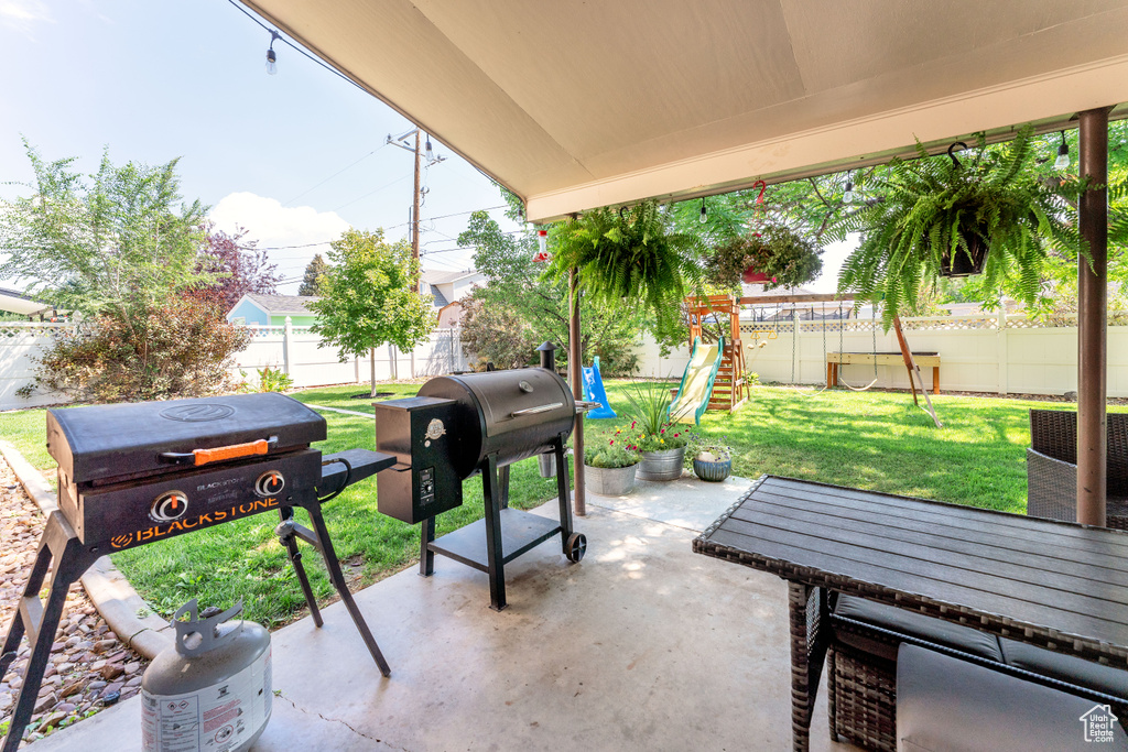 Fenced backyard featuring a playground, a patio area, and grilling area