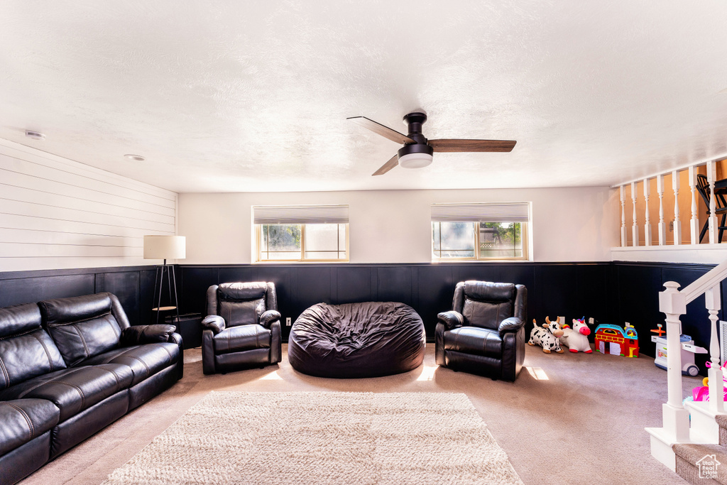 Carpeted living room with ceiling fan and wooden walls