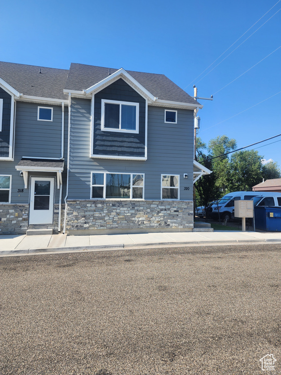 View of front of property featuring stone siding and roof with shingles