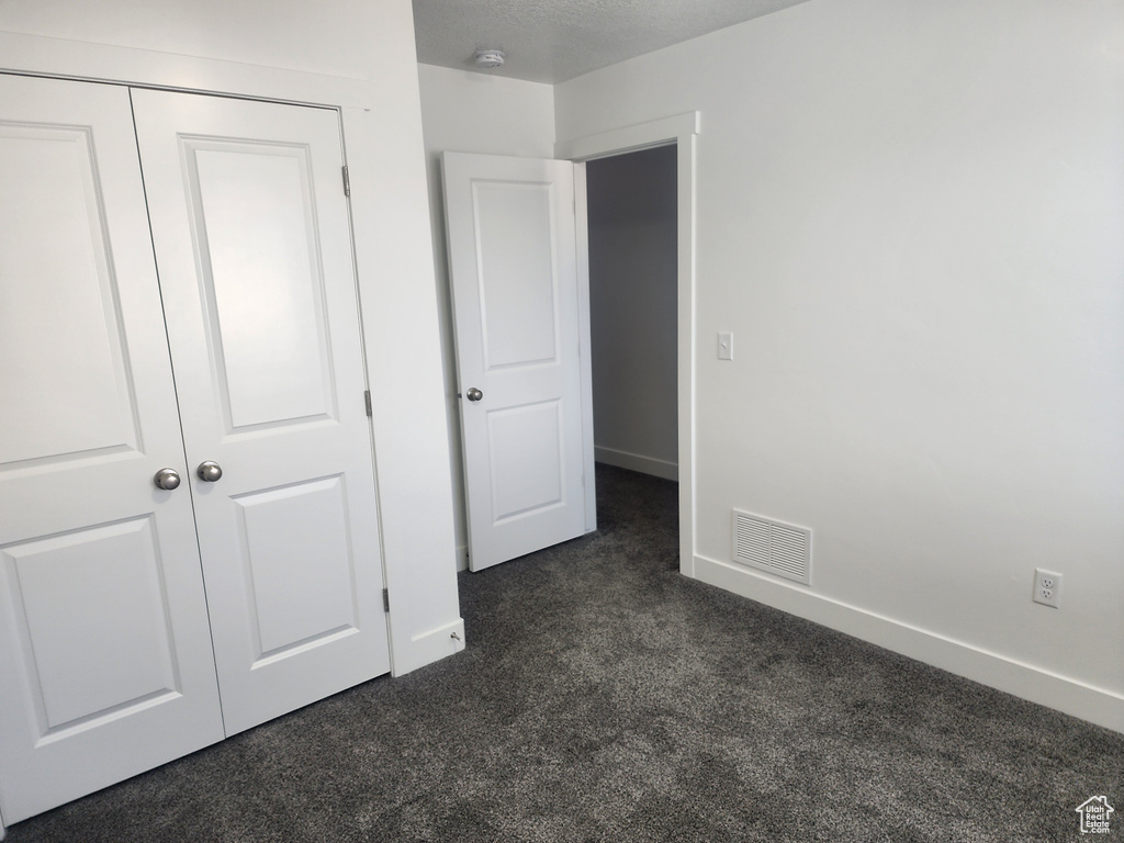 Unfurnished bedroom with dark carpet and a closet