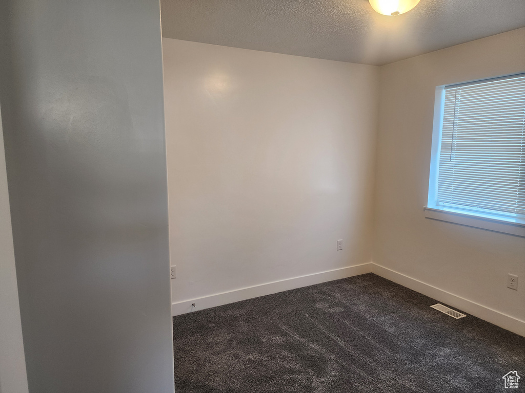 Unfurnished room featuring dark carpet and a textured ceiling