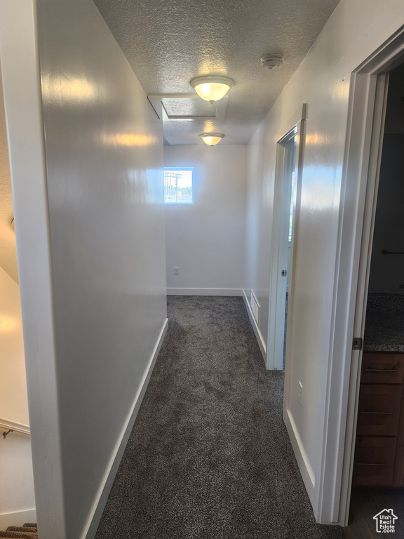 Hall featuring dark colored carpet and a textured ceiling