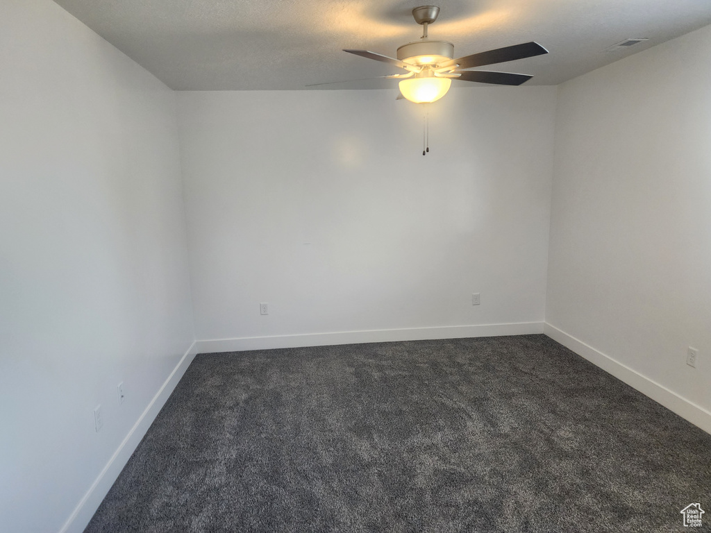 Spare room featuring dark colored carpet and a ceiling fan