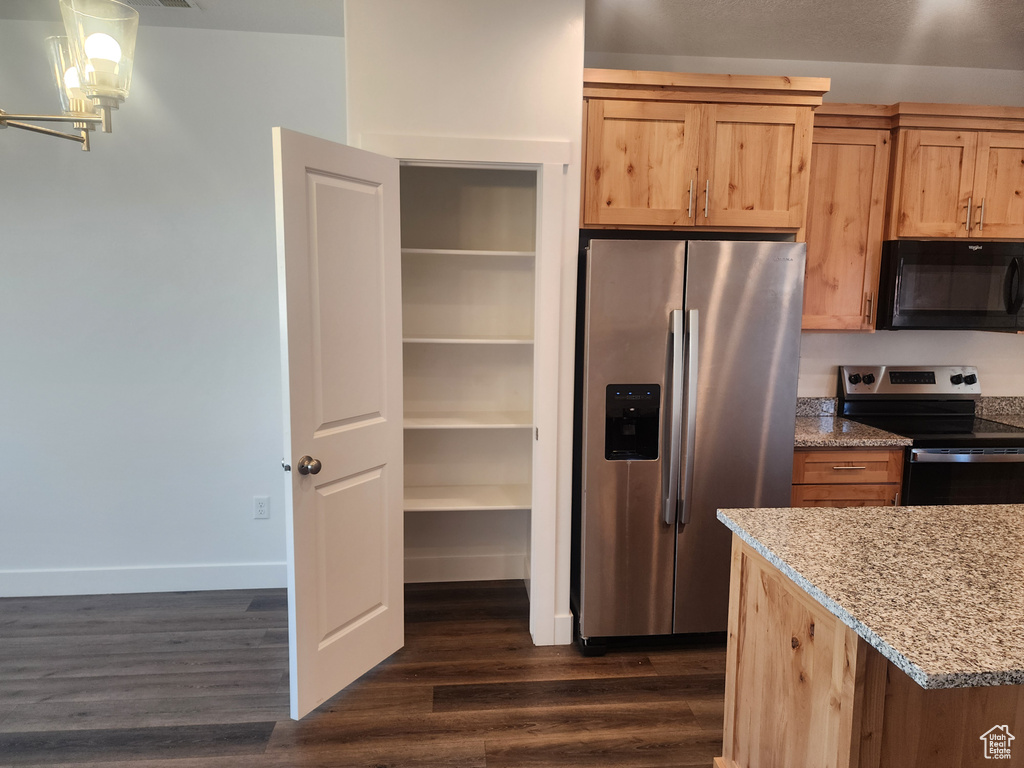 Kitchen with appliances with stainless steel finishes, dark wood-type flooring, light stone countertops, and a chandelier