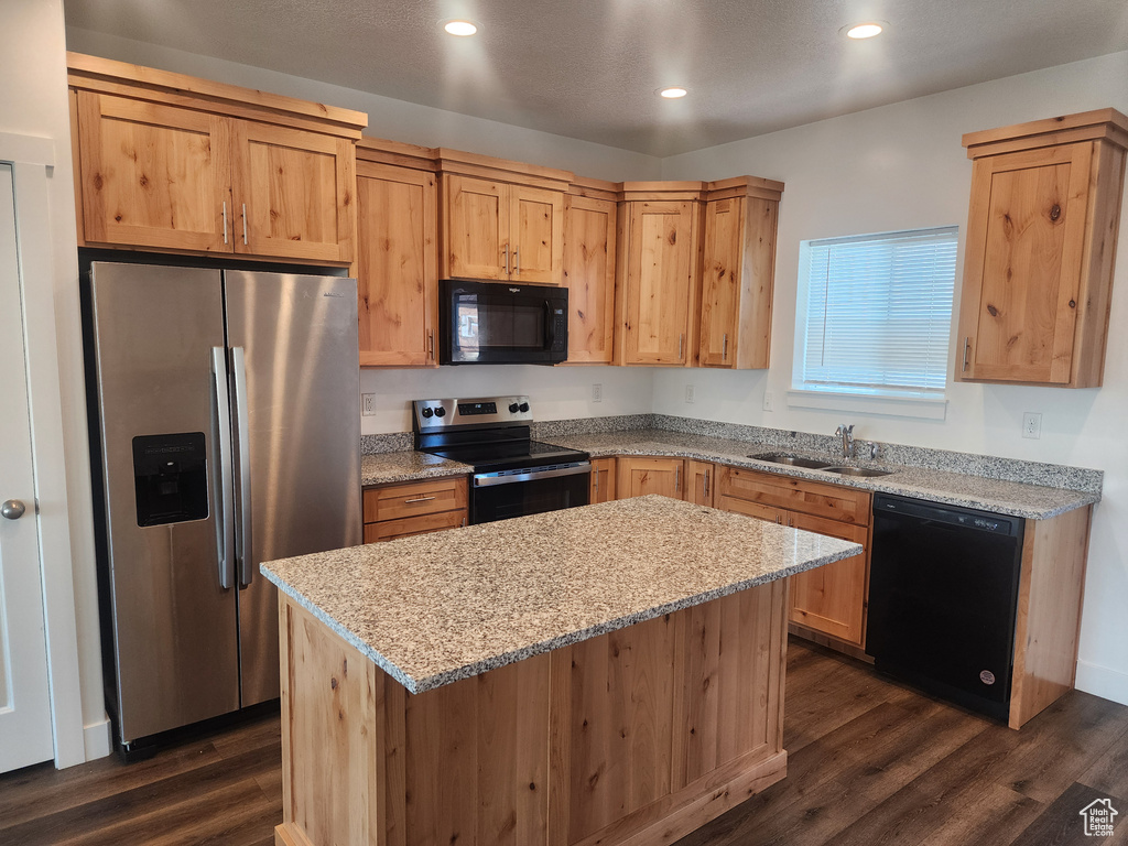 Kitchen featuring black appliances, dark wood finished floors, light stone counters, a kitchen island, and recessed lighting