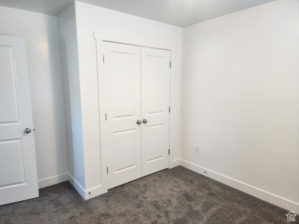 Unfurnished bedroom featuring dark carpet and a closet