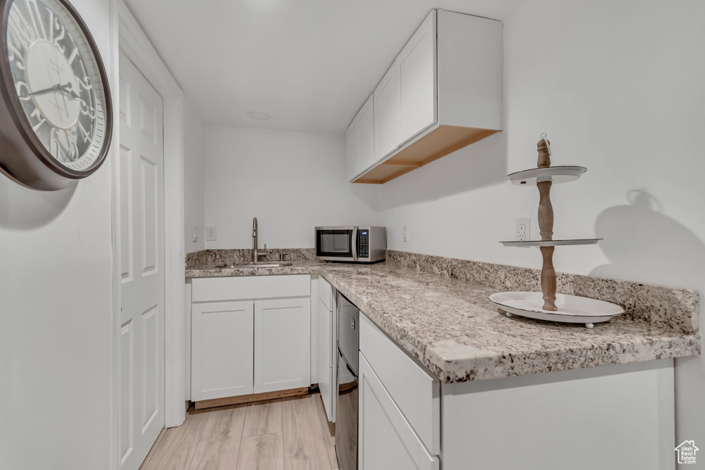 Kitchen with white cabinets, stainless steel microwave, light wood finished floors, and light stone countertops