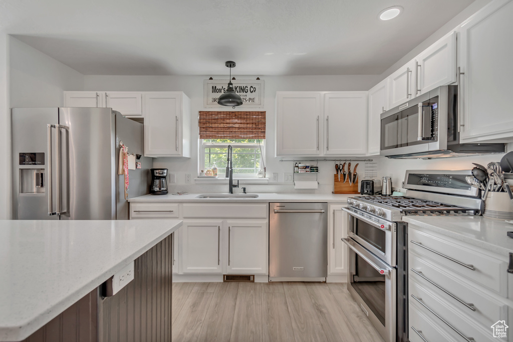 Kitchen featuring appliances with stainless steel finishes, white cabinetry, light wood finished floors, decorative light fixtures, and recessed lighting