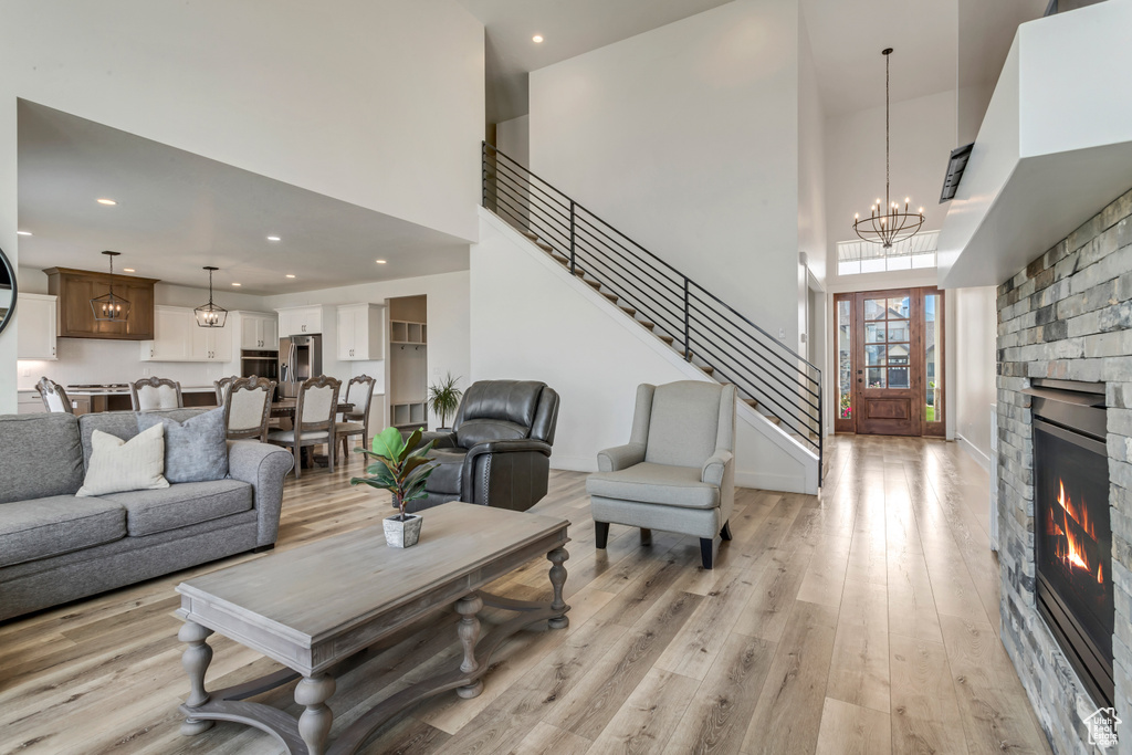 Living room featuring a towering ceiling, light wood finished floors, a glass covered fireplace, recessed lighting, and a chandelier