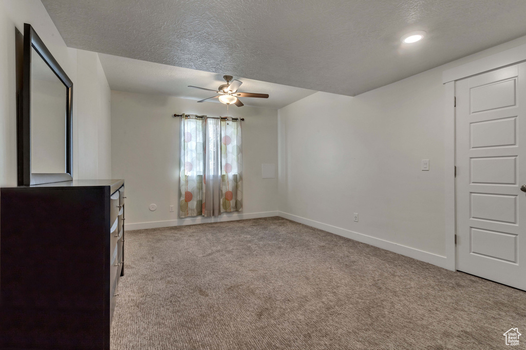 Unfurnished living room featuring ceiling fan, carpet, and a textured ceiling