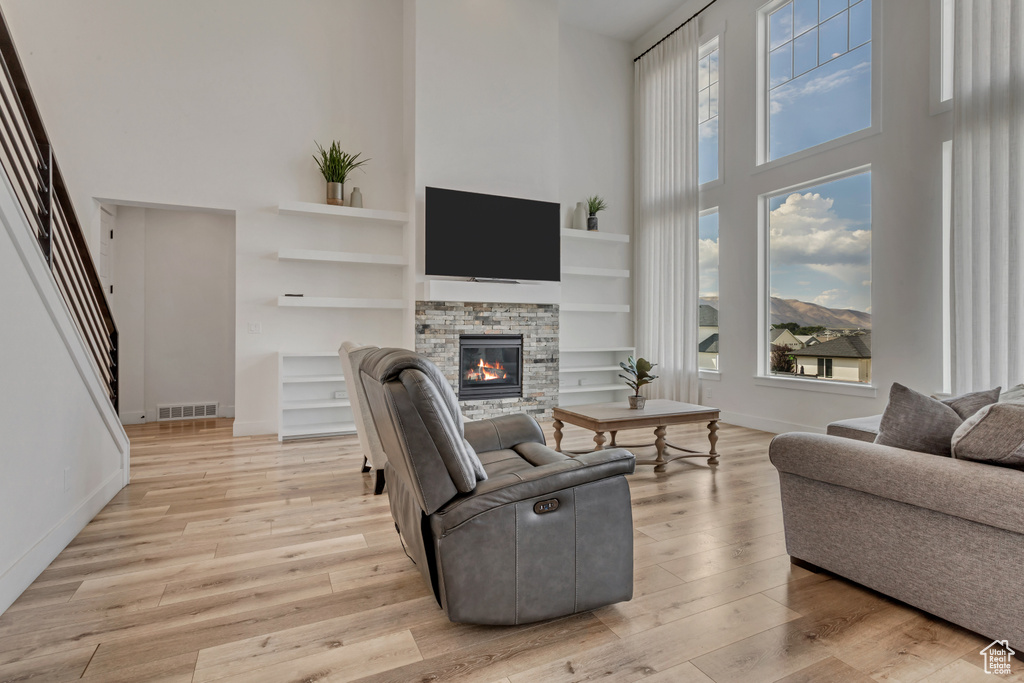 Living room featuring a high ceiling, a fireplace, plenty of natural light, light wood-style flooring, and built in shelves