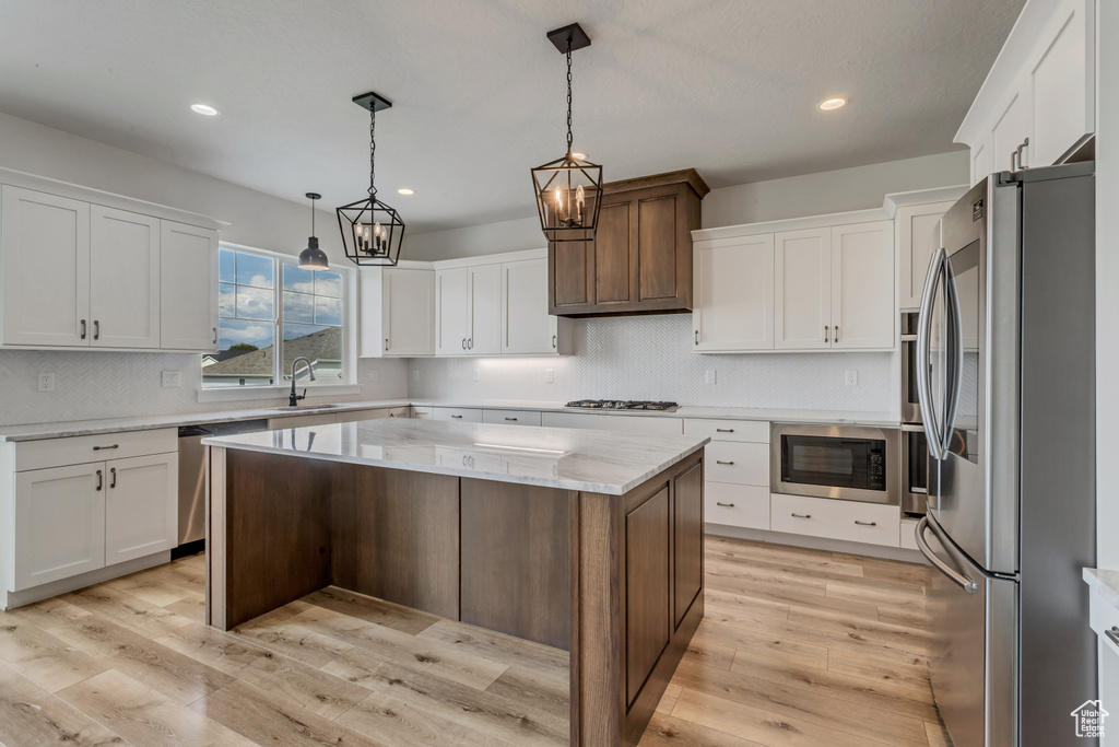 Kitchen with appliances with stainless steel finishes, white cabinets, backsplash, recessed lighting, and a center island