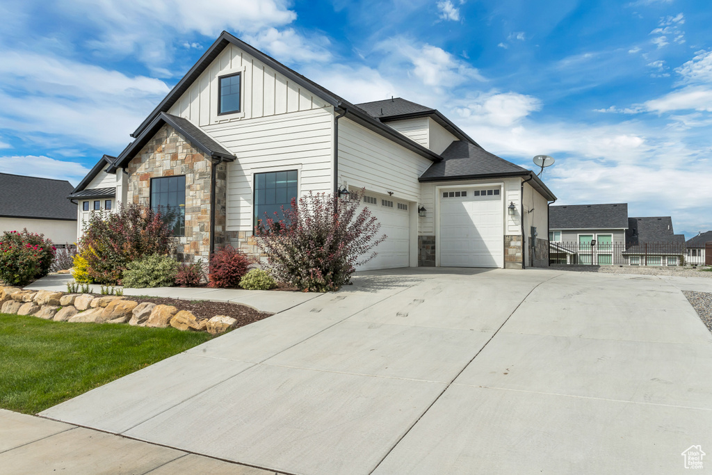 View of front facade with stone siding, an attached garage, board and batten siding, and driveway